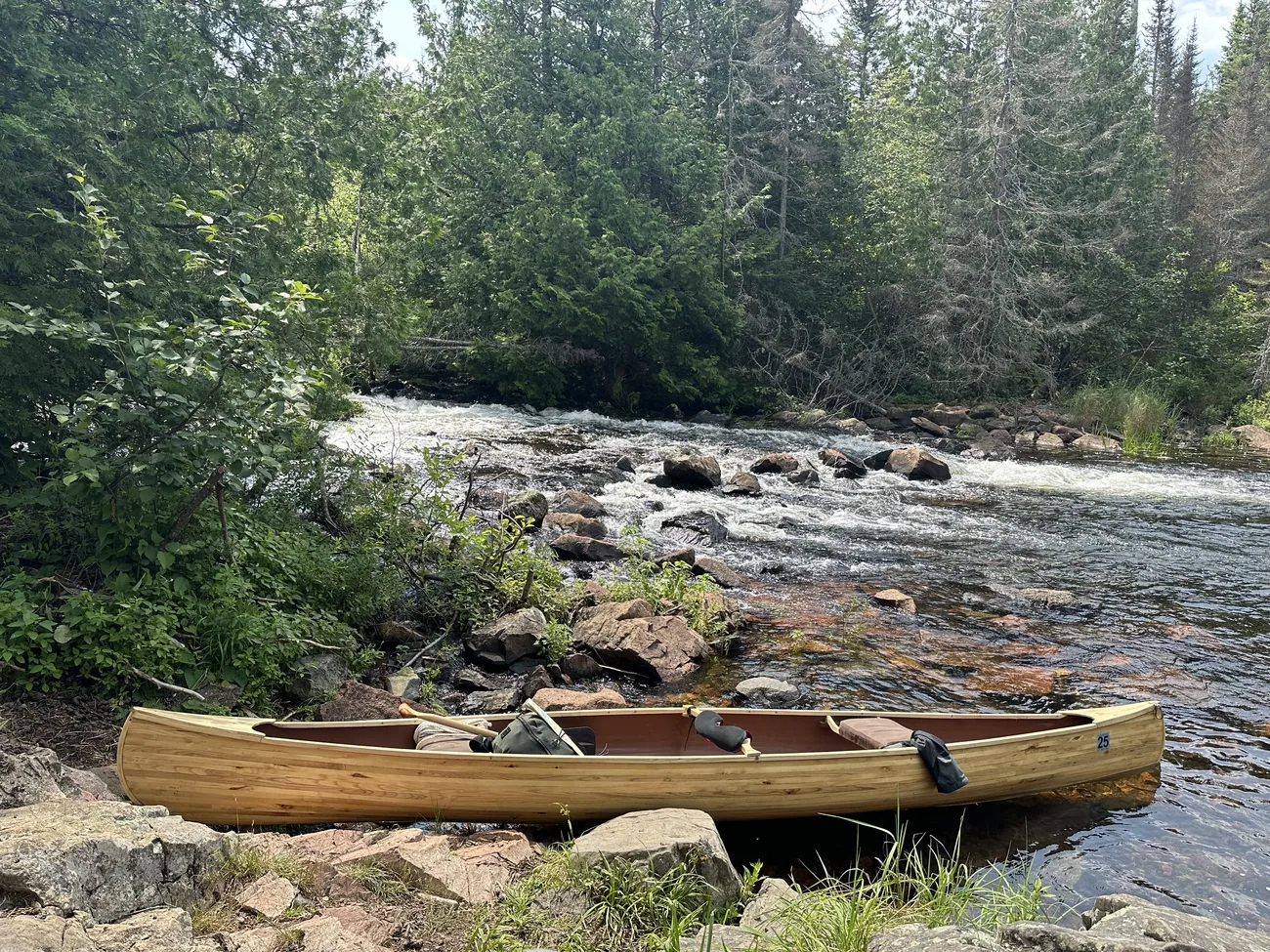 The canoe resting on rocks beside a set of rapids